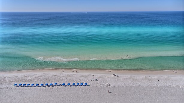 A beach with clear turquoise waters, a sandy shore, and a row of blue umbrellas.