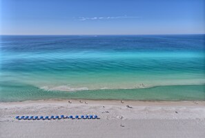 Ein Strand mit klarem türkisblauem Wasser, einem sandigen Ufer und einer Reihe blauer Sonnenschirme.