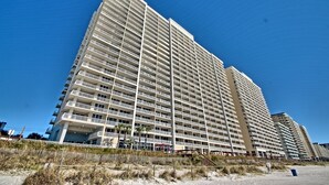 A high-rise hotel with multiple balconies, located near a beach.