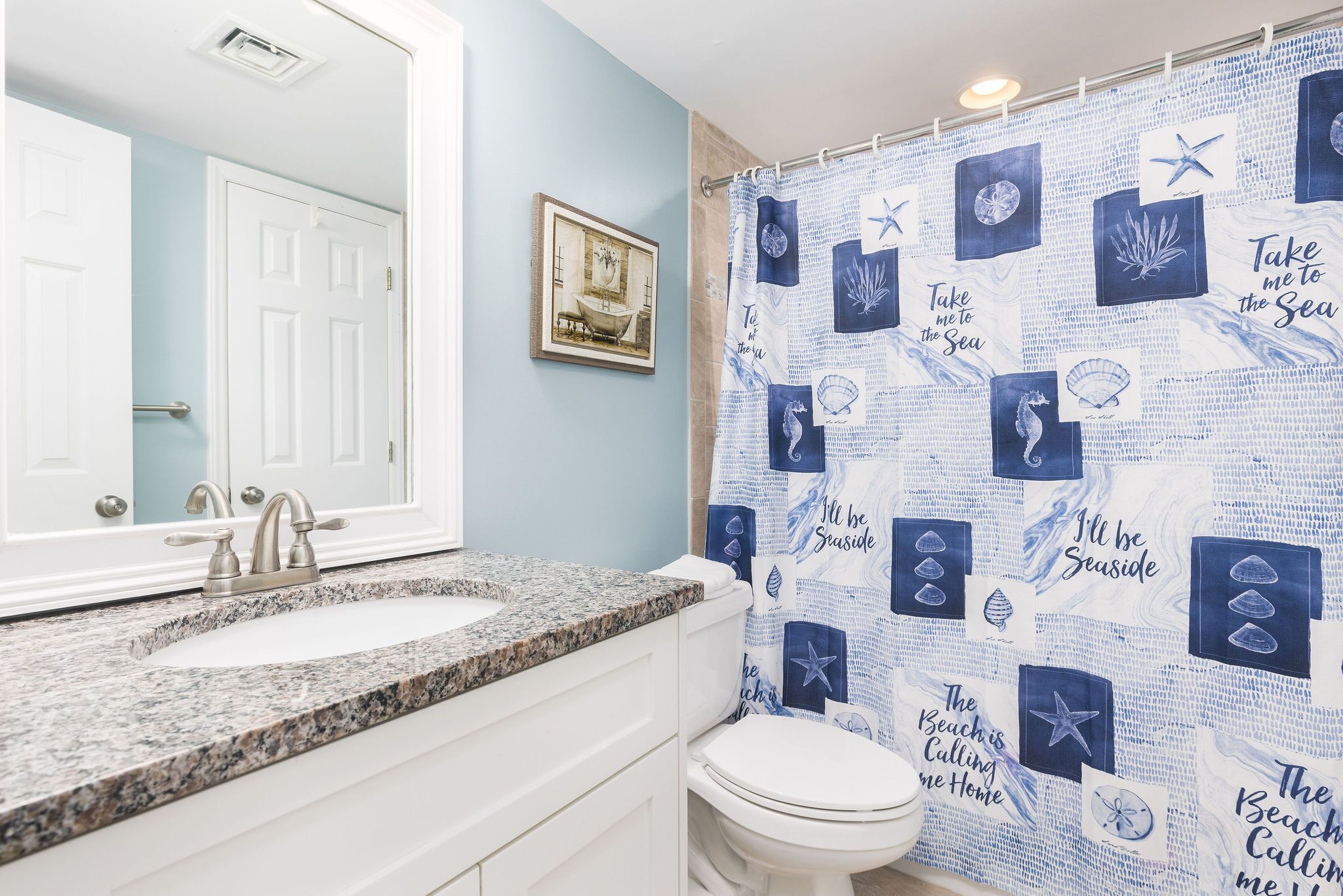 Een badkamer met een wastafelblad van graniet, een wit toilet en een douchegordijn met nautische motieven.