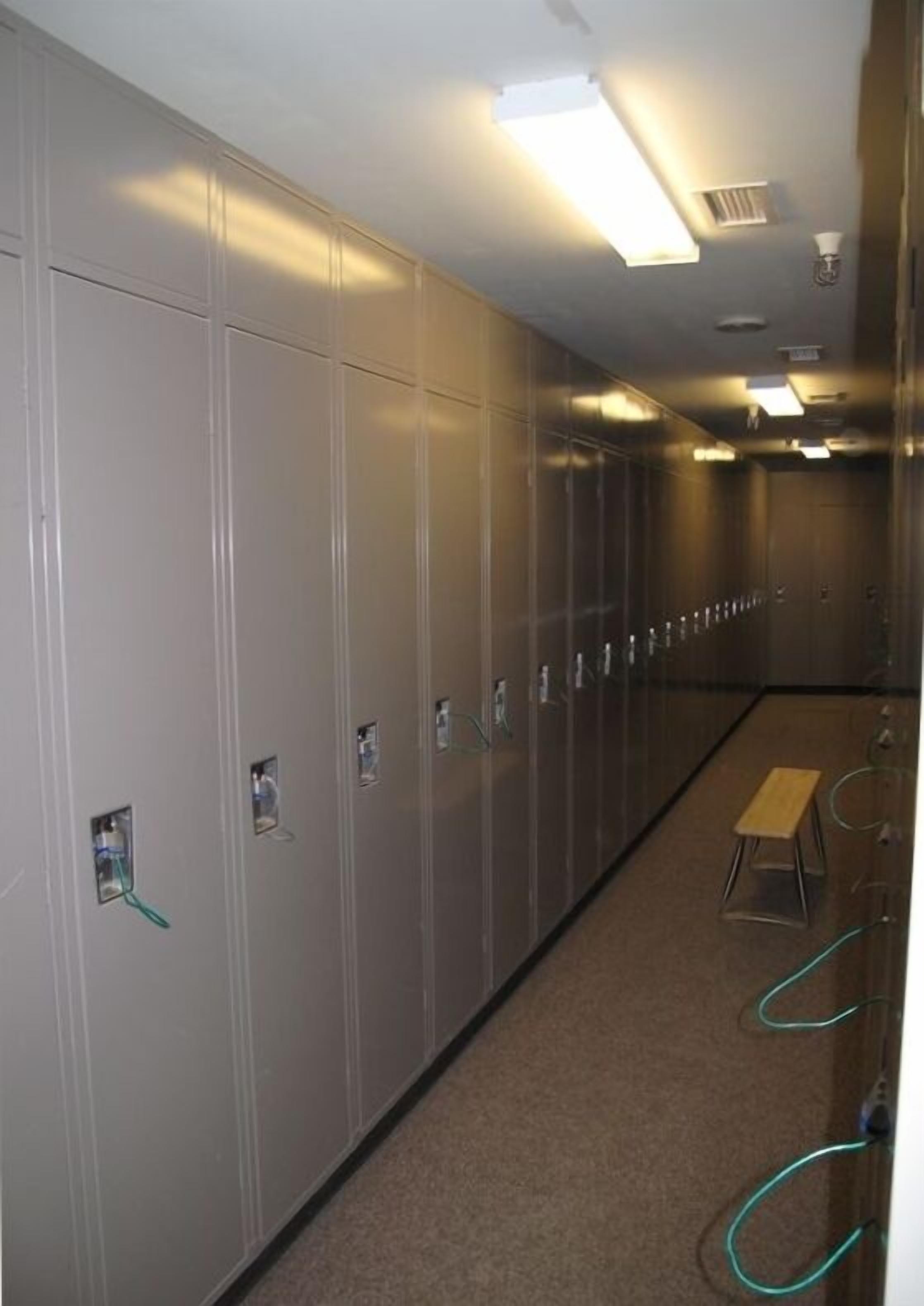 A long hallway with lockers, a bench, and a carpeted floor.