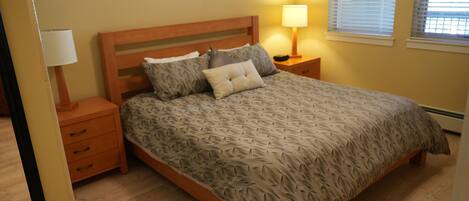 A bedroom with a wooden bed, a nightstand with a lamp, and a window with blinds.