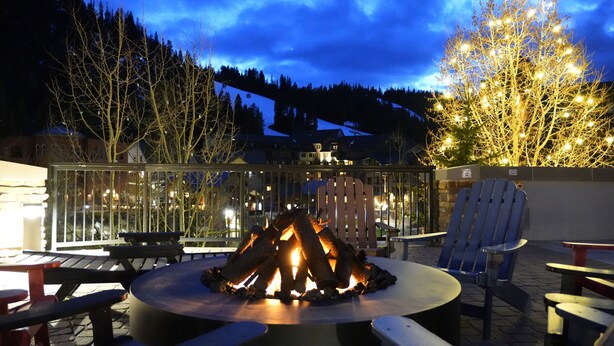 A fire pit surrounded by outdoor seating, a glass railing, and a view of a mountain and houses in the background. - 5th-Floor With Beautiful Views • Full Kitchen • Elegant New Italian Sleeper Sofa (Winter Park)