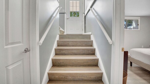 A staircase with wooden steps and white walls leading to a door with a window. - Beautiful and modern 3 bedroom, 1 bath Duplex.  Sleeps 6 (Chaffee)