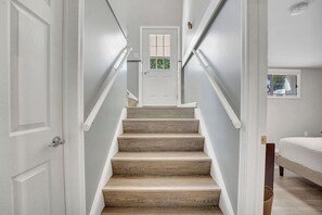 A staircase with wooden steps and white walls leading to a door with a window.