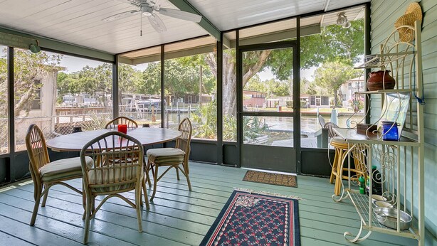 A covered patio with a table and chairs, large windows, and a ceiling fan.