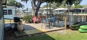 An outdoor patio with tables and chairs, a grill, kayaks, and a small building in the background. - HAVE IT ALL with floating dock, commercial icemaker and deepest canal in town! (Crystal River)