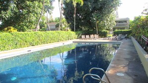 A rectangular swimming pool with a metal ladder on the right side, surrounded by a concrete deck.