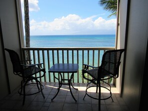 A balcony with two chairs and a table, overlooking a clear blue sea and a sailboat in the distance. - Maui is calling....it's a great time to take a trip! (Lahaina)