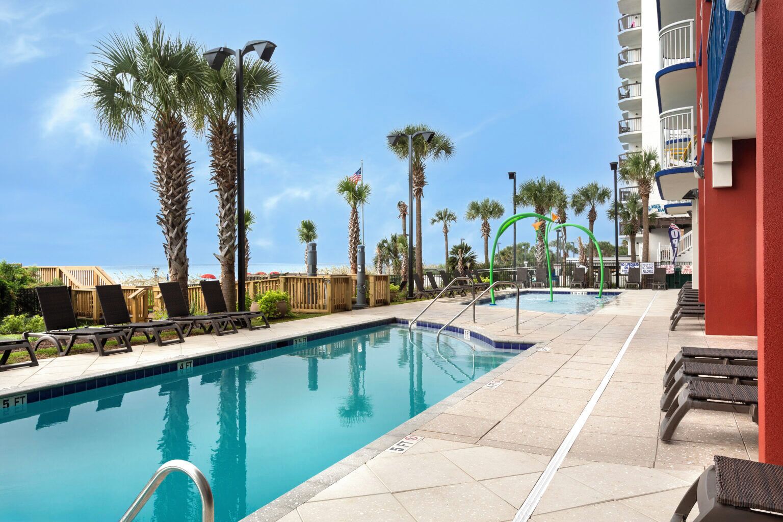 A pool area with lounge chairs, palm trees, and a building with balconies.