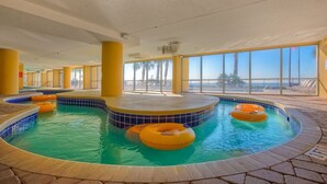Una piscina interior con varias pistas, pilares amarillos y vistas despejadas de la playa a través de amplias ventanas.