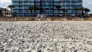 Un hotel de gran altura con varios balcones, una playa en primer plano y un cielo despejado.