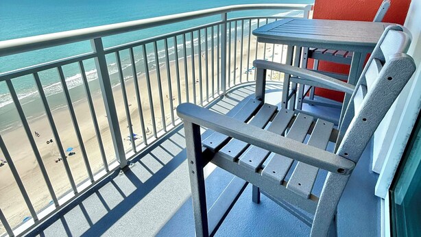 Un balcón con vista a la playa, una mesa y una silla.