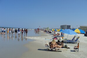 Una playa con gente caminando y sentada bajo sombrillas.