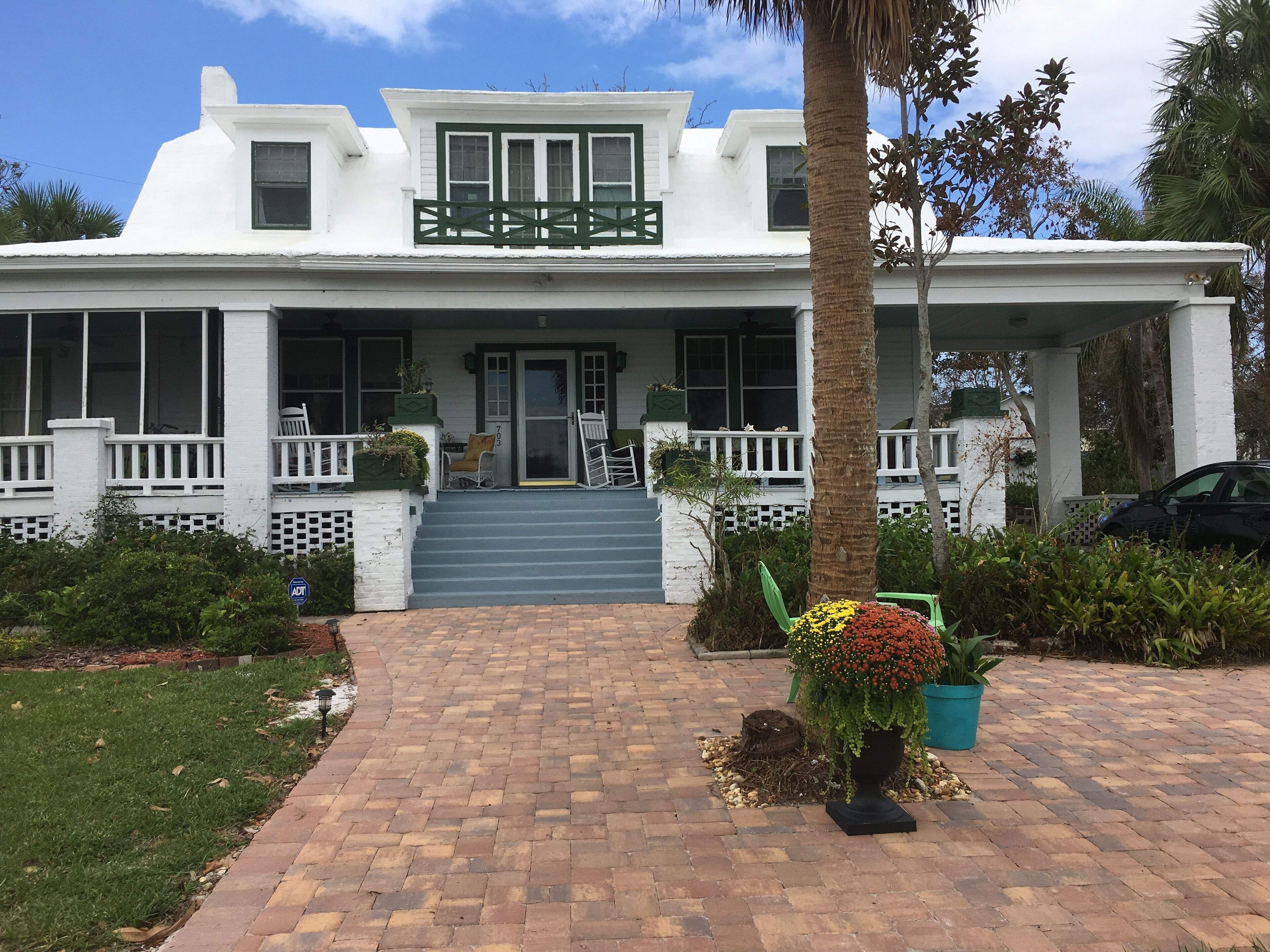 A white house with a porch, steps leading to the entrance, and a potted plant in the foreground.