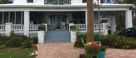 A white house with a porch, steps leading to the entrance, and a potted plant in the foreground.