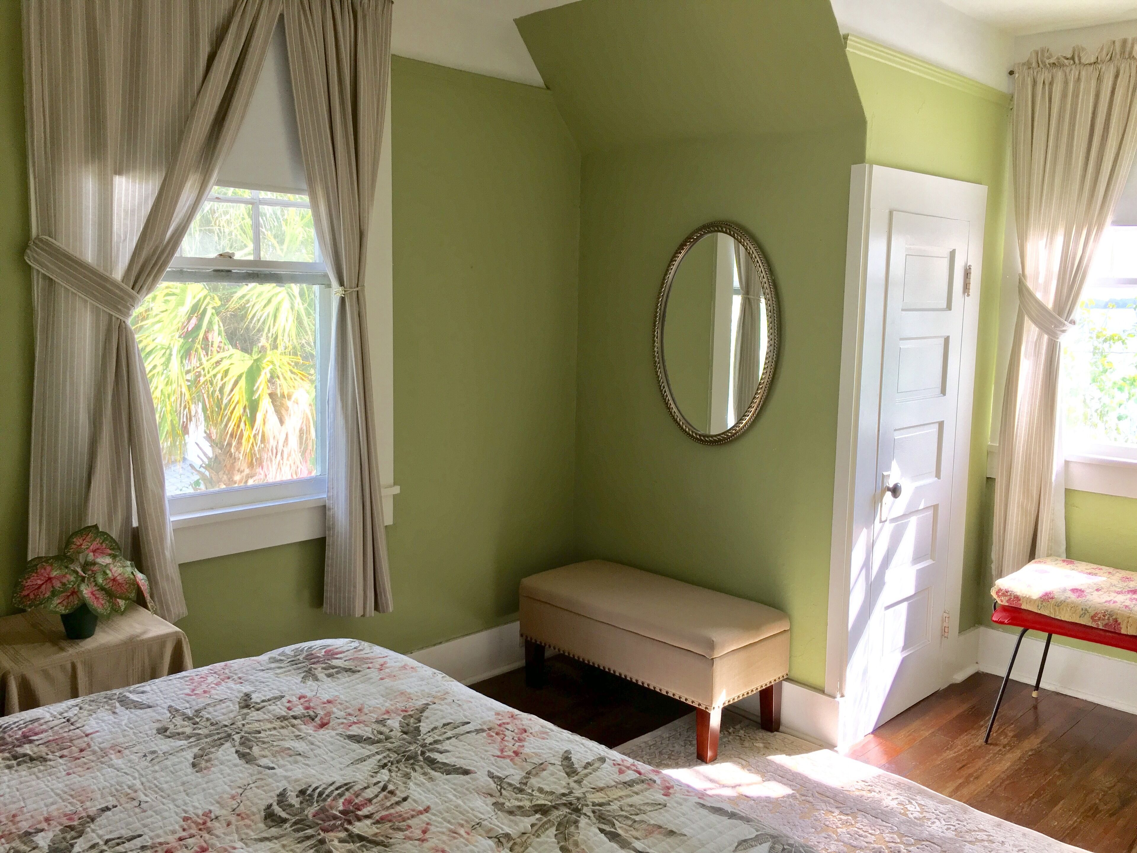 Una habitación con cama, un banco, un espejo y una puerta.