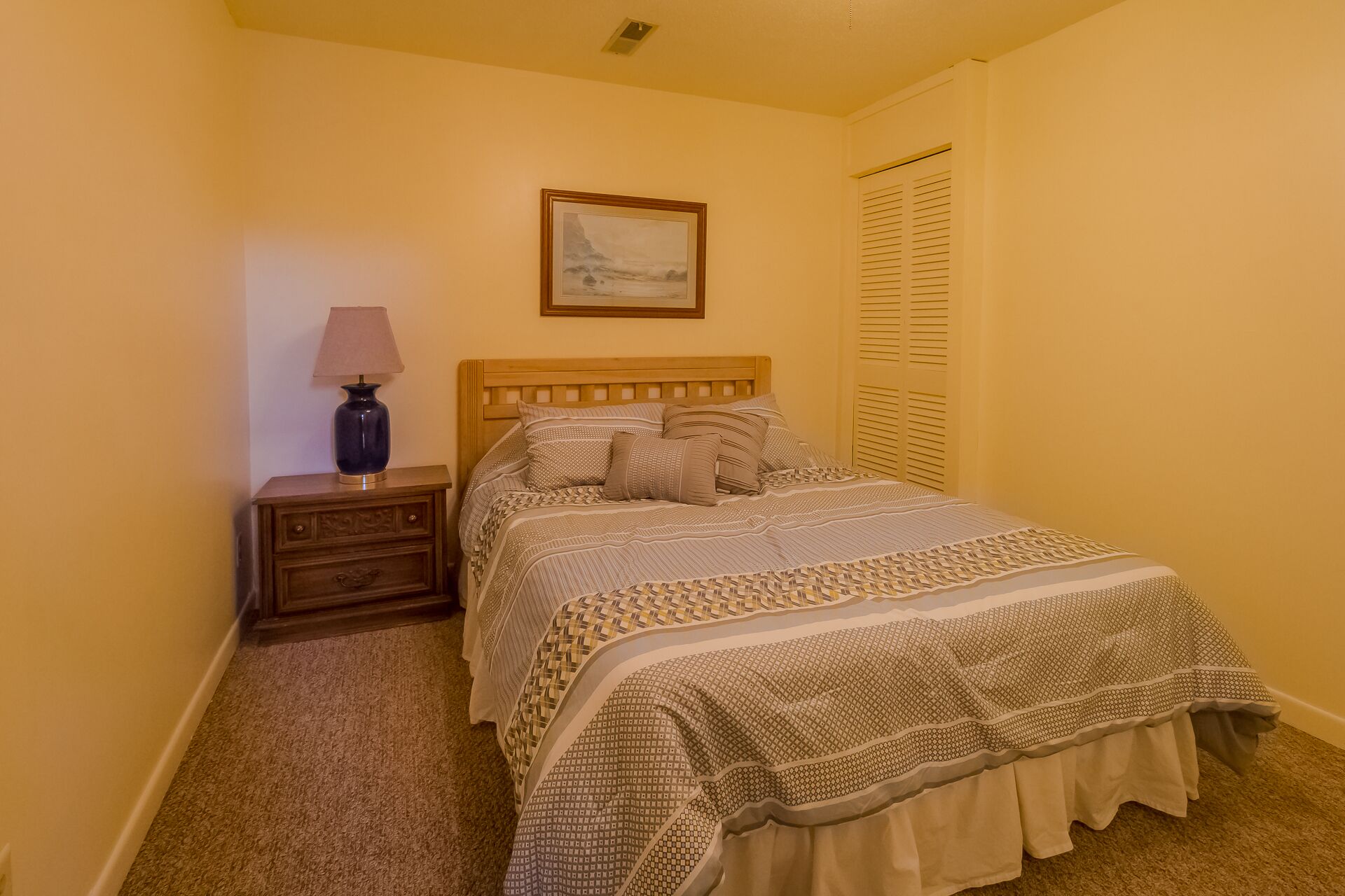 Une chambre à coucher avec un lit en bois, une table de chevet avec une lampe, un tableau encadré au mur et une fenêtre avec des stores.