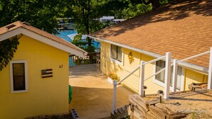 Ein gelbes Gebäude mit der Nummer 47 an der Wand, einer kleinen Veranda und Blick auf einen Steg sowie Boote im Hintergrund.