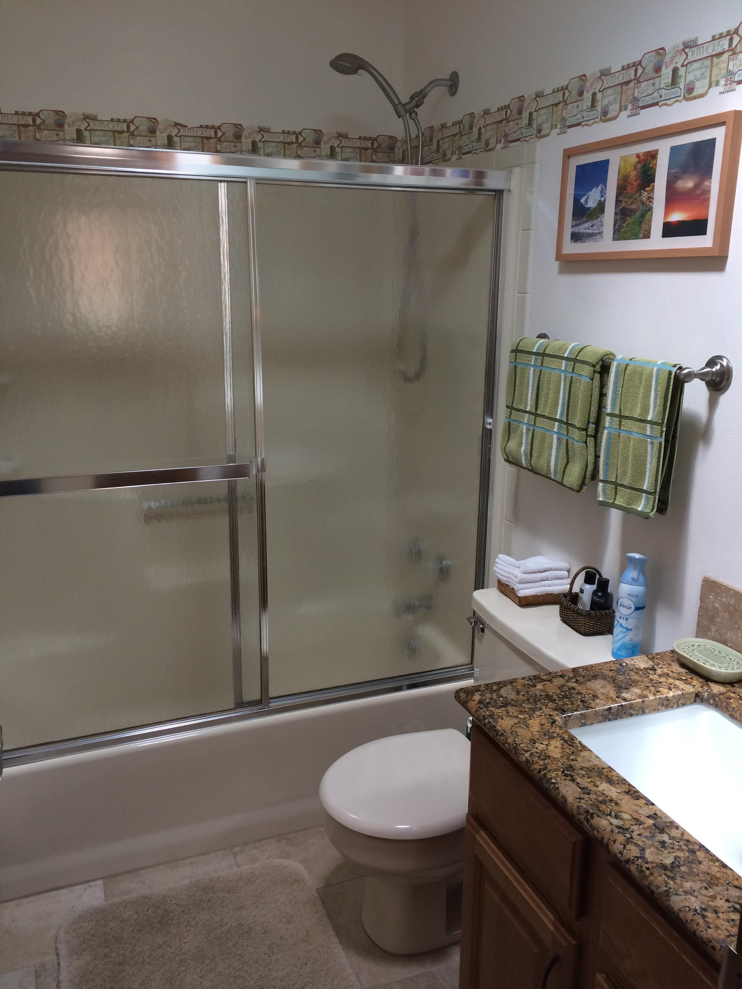 A bathroom with a glass-enclosed shower, a toilet, a sink with a granite countertop, and a towel rack with green towels.