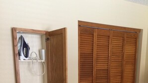 Een kamer met een inbouwstrijkplank, een houten garderobe en een kamerkleed met dessin.