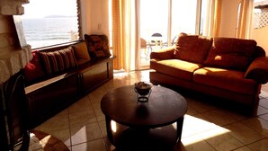 Una sala de estar con sofá, una mesa de centro y vista al mar a través de una ventana.