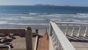 Una escalera que baja a una playa, con barandilla y plantas en macetas.