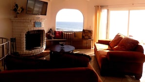 Una sala de estar con chimenea, un sofá, una mesa de centro y vista al mar a través de un ventanal.