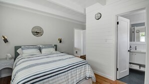 A bedroom with a bed, bedside tables, a nightstand, a wall clock, and a door leading to a bathroom. - Oceanfront At Stinson - Relax And Refresh (Stinson Beach)