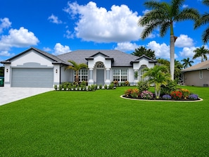 A residential house with a garage, a well-maintained lawn, and a variety of tropical plants.