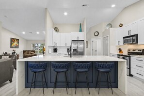 A modern kitchen with a central island, bar stools, stainless steel appliances, and white cabinetry.