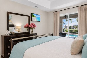 A hotel room with a bed, a TV, a desk with a lamp, a mirror, and a view of a pool.