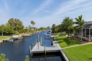 A canal with boats docked, surrounded by greenery and a building with a modern design.
