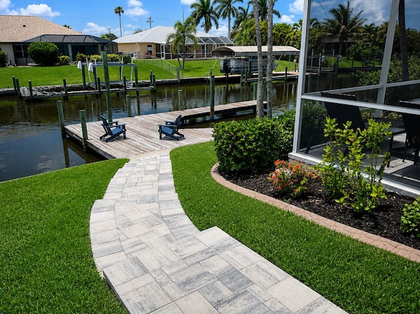 A marina with a paved walkway, docked boats, and a grassy area with small shrubs.