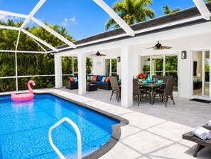 A pool area with a clear blue pool, a pink flamingo float, and a dining area with a table and chairs.