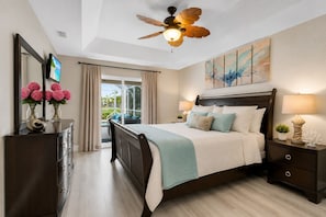 A bedroom with a bed, a nightstand, a dresser, a ceiling fan, and a view of the outdoors.