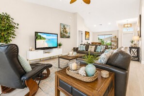 A modern living room with a television, leather sofas, a coffee table, and a large window.
