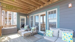 Eine überdachte Veranda mit Holzboden, einer Couch mit gemusterten Kissen und einem Fenster mit Blick auf ein Gebäude.