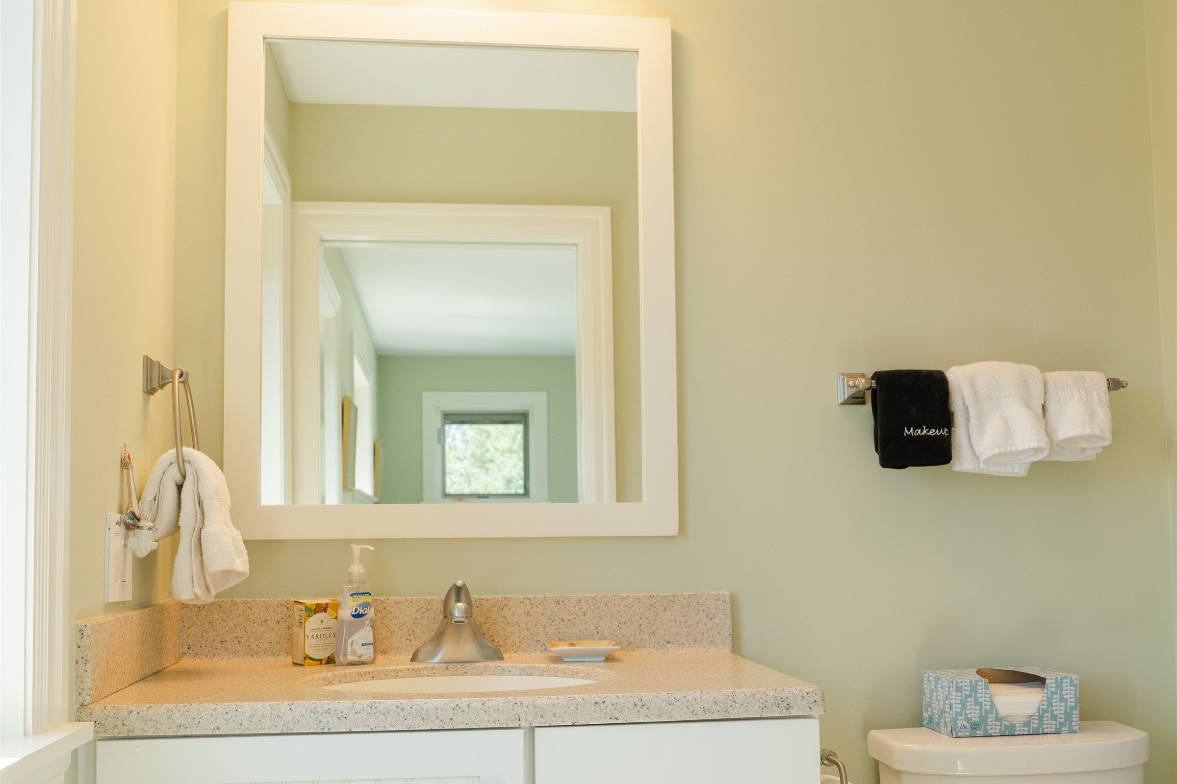Une salle de bain avec un grand miroir, un lavabo avec un robinet, des toilettes et un porte-serviettes avec des serviettes.