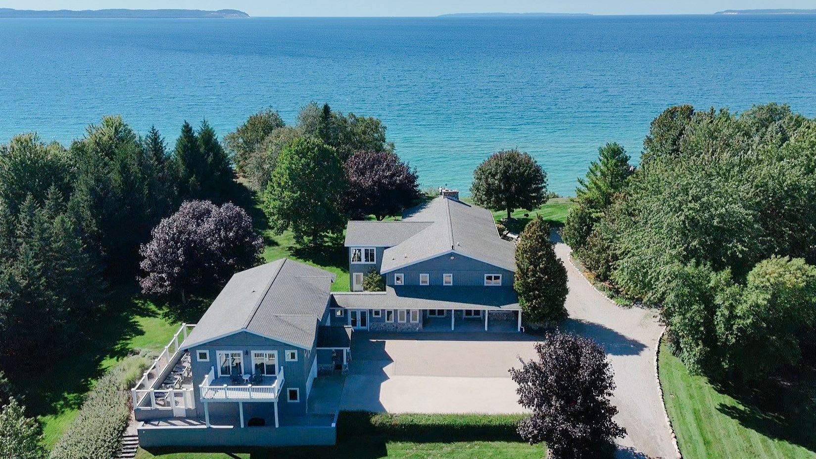 Una casa grande con un amplio camino de entrada, rodeada de árboles y vista al mar.
