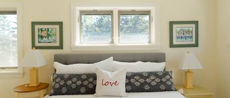 Ein Schlafzimmer mit einem Bett, zwei Nachttischen, zwei Lampen, einem Fenster und zwei gerahmten Bildern an der Wand.