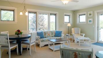 A cozy room with a round table, white chairs, a floral sofa, and a ceiling fan.