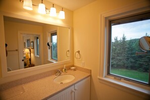 A bathroom with a sink, mirror, and window with a view of trees. - Rent Two Suites On A Beautiful Five Acre Estate (Leland)