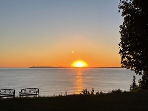 A sunset over a calm body of water with two benches facing the view. - Rent Two Suites On A Beautiful Five Acre Estate (Leland)