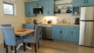 A kitchen with blue cabinets, a stainless steel refrigerator, a dishwasher, and a dining area with patterned chairs.