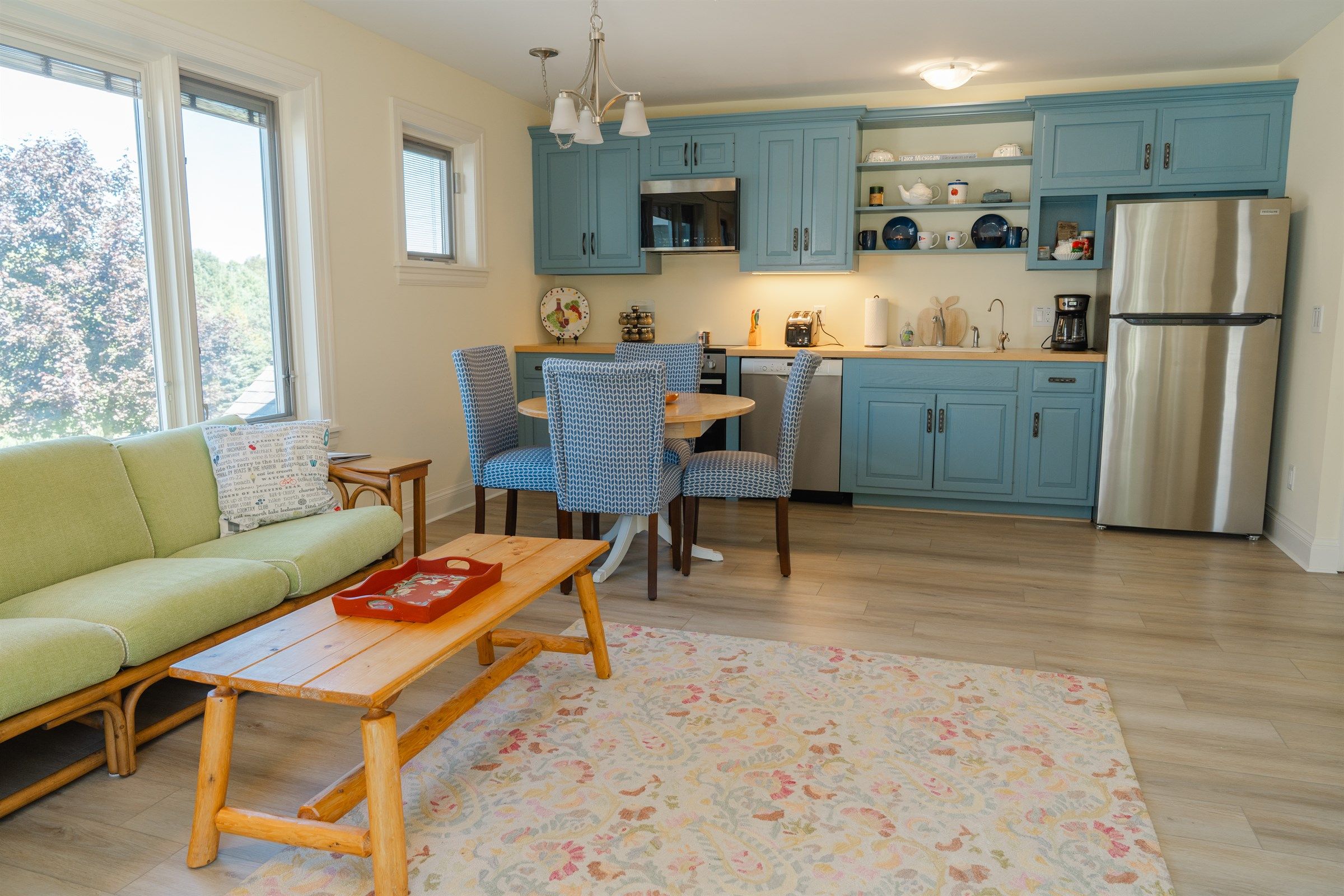 Een moderne keuken met blauwe kastjes, een roestvrijstalen koelkast en een eethoek met gestreepte stoelen.