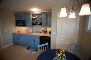 A kitchen with blue cabinets, a microwave, a coffee maker, and a sink. There is a dining table with chairs and a vase of flowers. - Rent Two Suites On A Beautiful Five Acre Estate (Leland)
