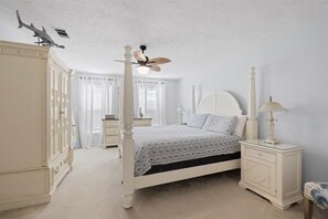 A bedroom with a four-poster bed, a ceiling fan, a nightstand with a lamp, and a wardrobe.