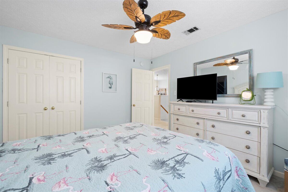 A bedroom with a bed, a dresser, a ceiling fan, a television, and a mirror.