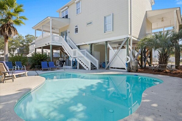 A swimming pool with a covered deck, a staircase, and lounge chairs.